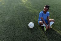 A footballer sitting on the pitch beside the ball during a break in play