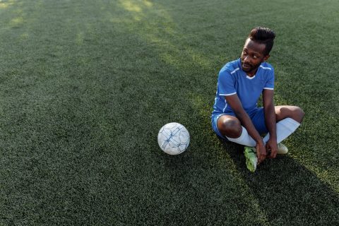 A footballer sitting on the pitch beside the ball during a break in play