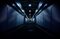 Long corridor lined with closed metal roller shutters under ceiling lights