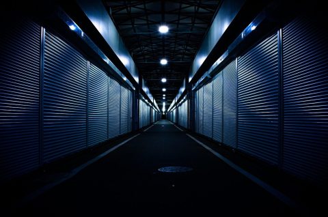 Long corridor lined with closed metal roller shutters under ceiling lights